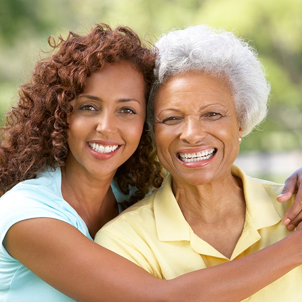 A teenage girl is hugging her grandmother in the park while they're smiling